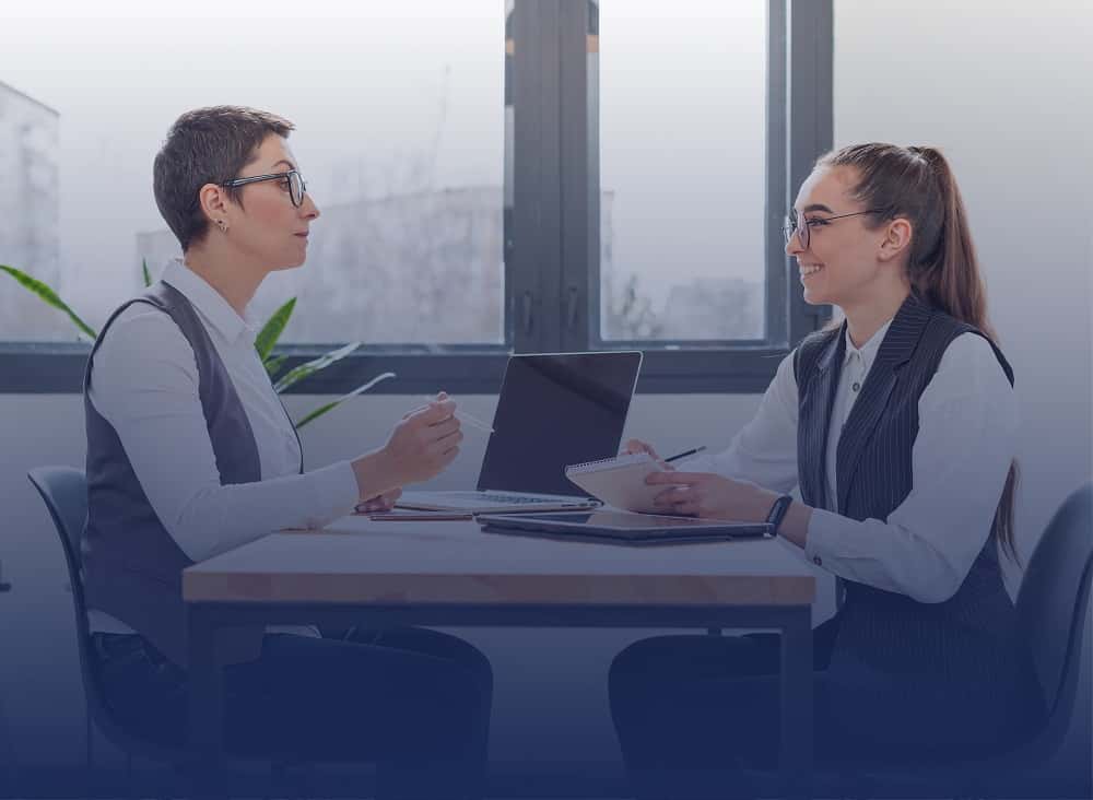 Two professionals discuss Divisive Debate Topics like climate change, AI ethics, remote work, gender equality, and education reform in an office setting.